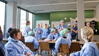 Ett trettiotal vårdklädda operationsmedarbetare fikar i en matsal