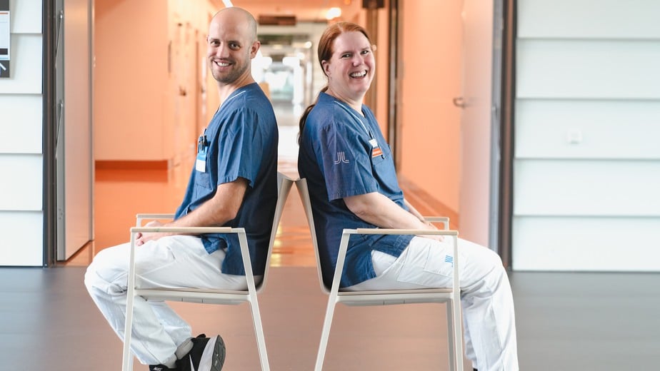 Niklas och Helena sitter mitt i en korridor i varsin stol med ryggarna mot varandra.