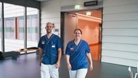 Niklas och Helena kommer gående mot kameran i sina blåvita sjukhuskläder.
