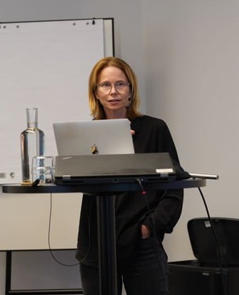 Ann-Charlotte Lindström föreläser i svarta jeans och svart tröja. Hon har blont hår till axlarna och glasögon.