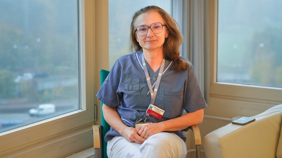 Kvinna med glasögon sitter i en fåtölj framför ett stort fönster.