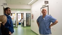 Två män i vårdkläder står och pratar i en sjukhuskorridor.