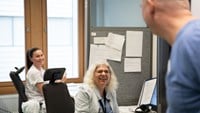 Två sjuksköterskor som sitter och arbetar vid sina datorer hejar glatt på sjukhusdirektör Christophe Pedroletti som tittar in.