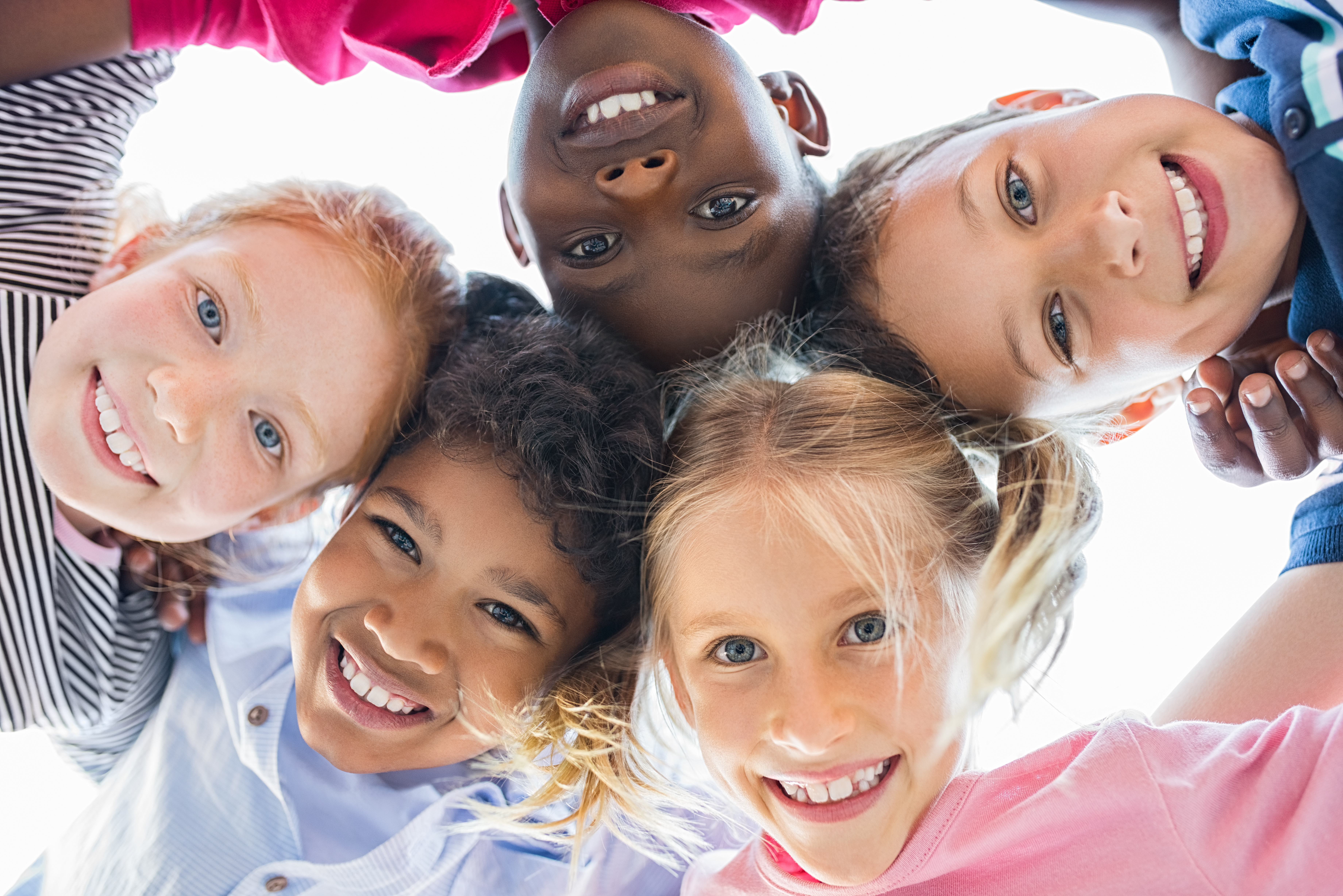 Closeup face of happy multiethnic children embracing each other and smiling at camera. Team of smiling kids embracing together in a circle. Portrait of young boy and pretty girls looking at camera.