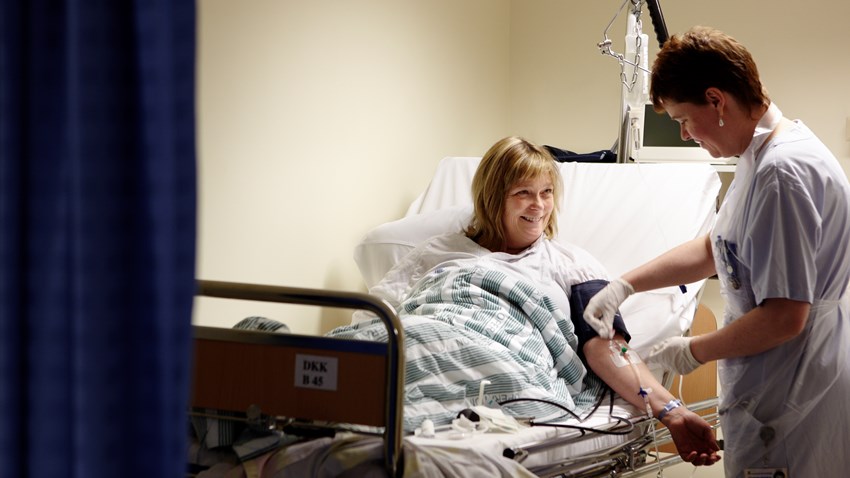 A patient, lying in a patient bed, and is being treated by health care professionals.
