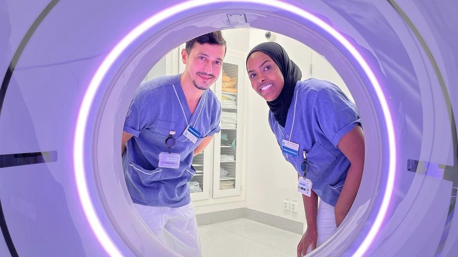 Kai Wejdan och Muna Osman ler och kikar in genom det stora runda hålet i röntgenapparaten