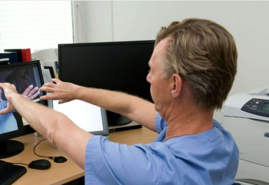 the image shows a man in a blue t-shirt holding his hands out towards a computer screen. 