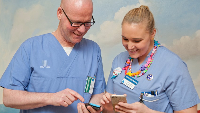 the image shows as man and a woman in blue hospital clothes. Both are looking at their mobile phones.