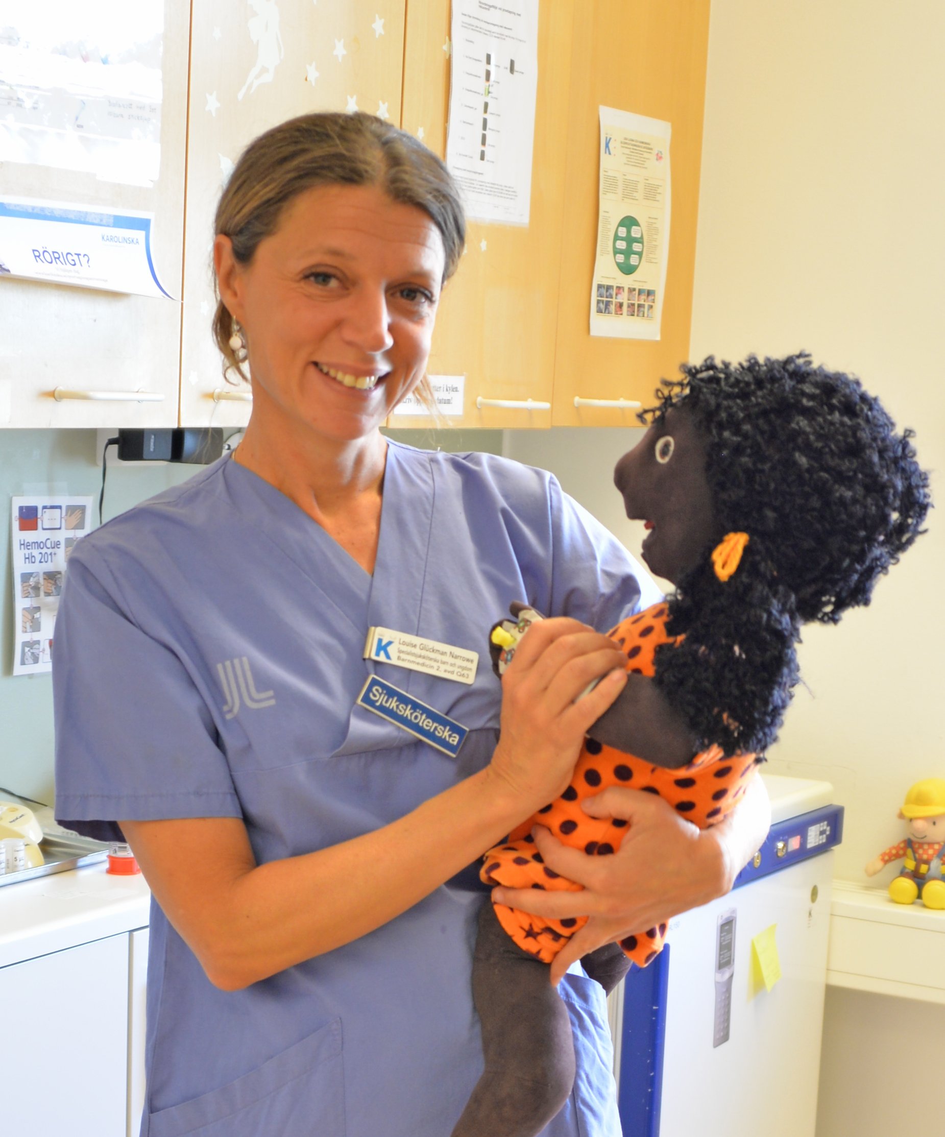 Barnsjuksköterska håller i docka som kan användas för att visa hur en behandling går till.