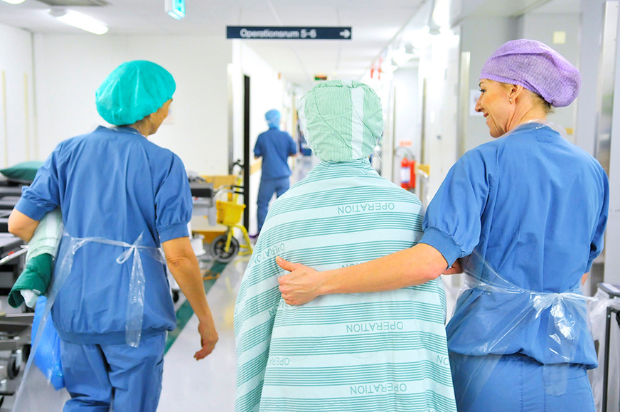 två vårdklädda personer leder en patient 