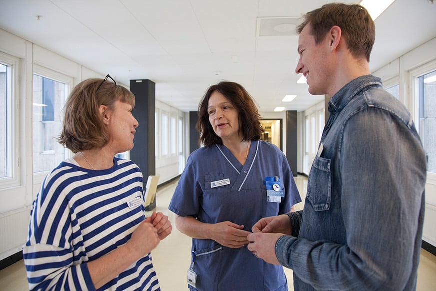Tre personer står i en vårdkorridor och pratar med varandra