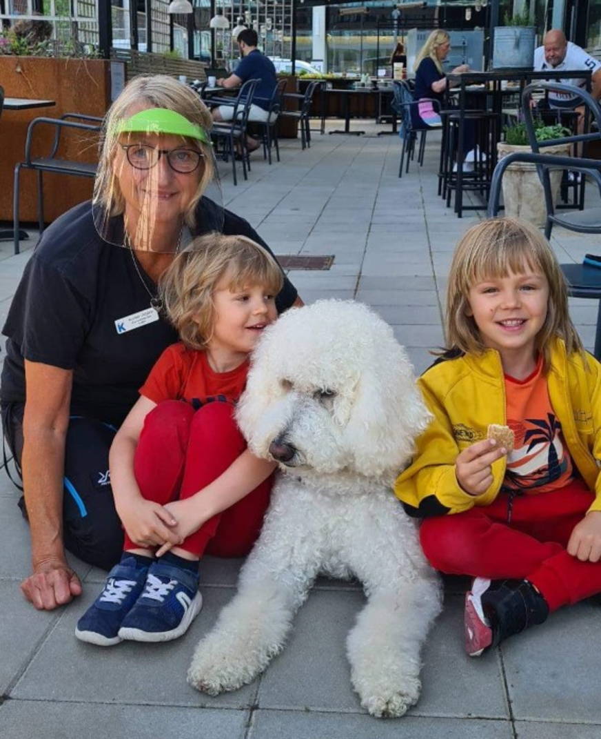 Sjuksköterska och två barn med vit hund ler mot kameran