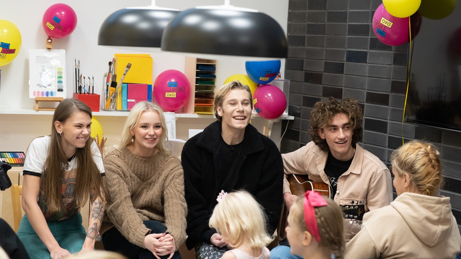 Idolerna sitter på rad framför barnen i ateljén och sjunger och skrattar.