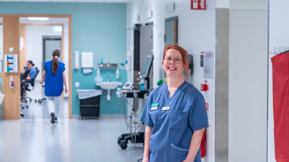 Sjuksköterska som står i en vit korridor.