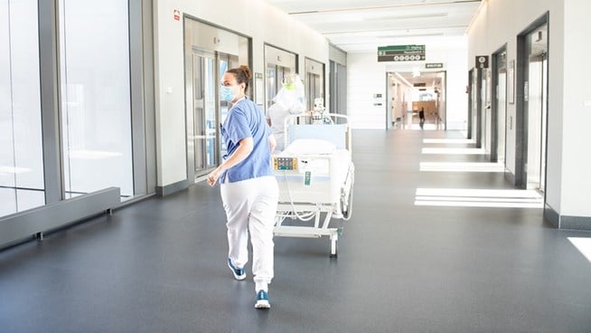 Vårdpersonal går med patientsäng i en korridor