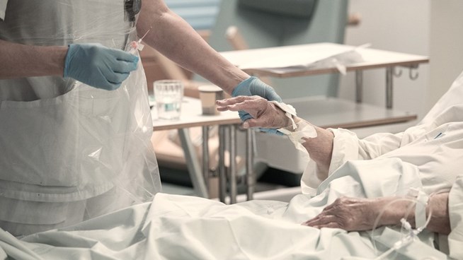 Vårdpersonal står vid patients säng och håller i handen